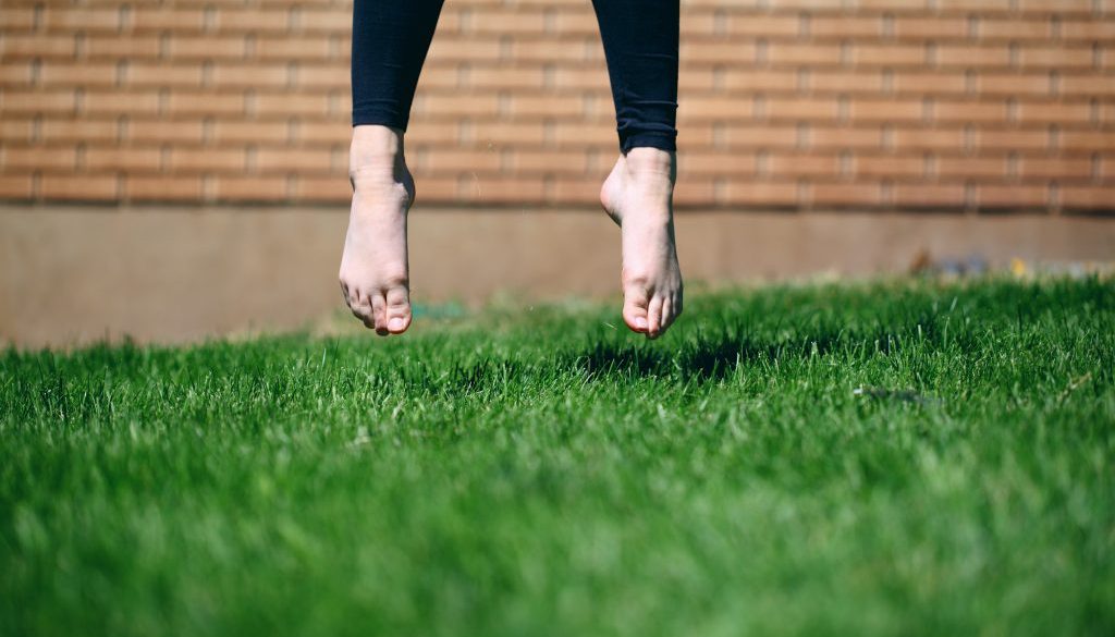 A person takes flight, barefoot in the green summer grass.