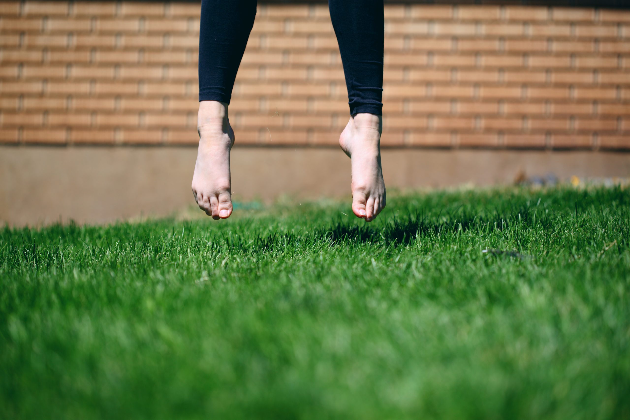 A person takes flight, barefoot in the green summer grass.